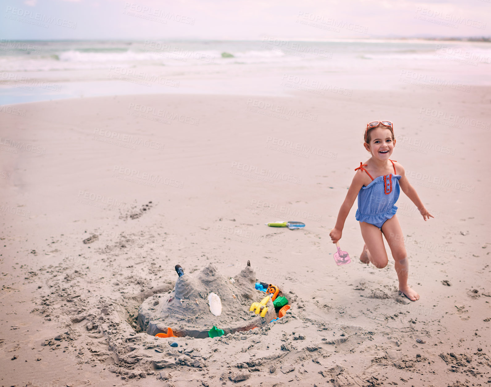 Buy stock photo Portrait, beach and little girl running with sandcastle outdoor by sea or ocean for carefree fun. Nature, water and energy with happy young child playing on sand at coast for holiday or vacation