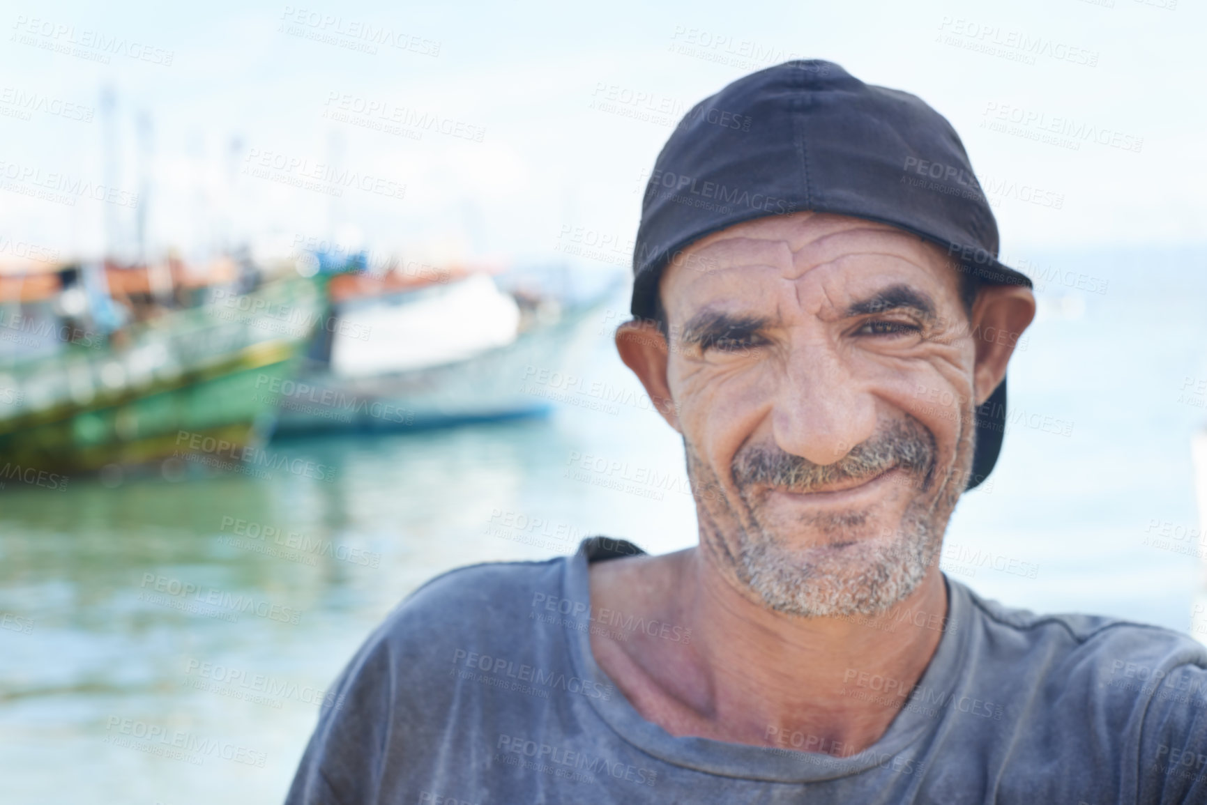 Buy stock photo Fisherman, portrait and rugged man with smile, boats and fishing trawler in ocean. Wrinkles, aged and mature happy male from Brazil, close up and self employed with nomadic lifestyle on the water 