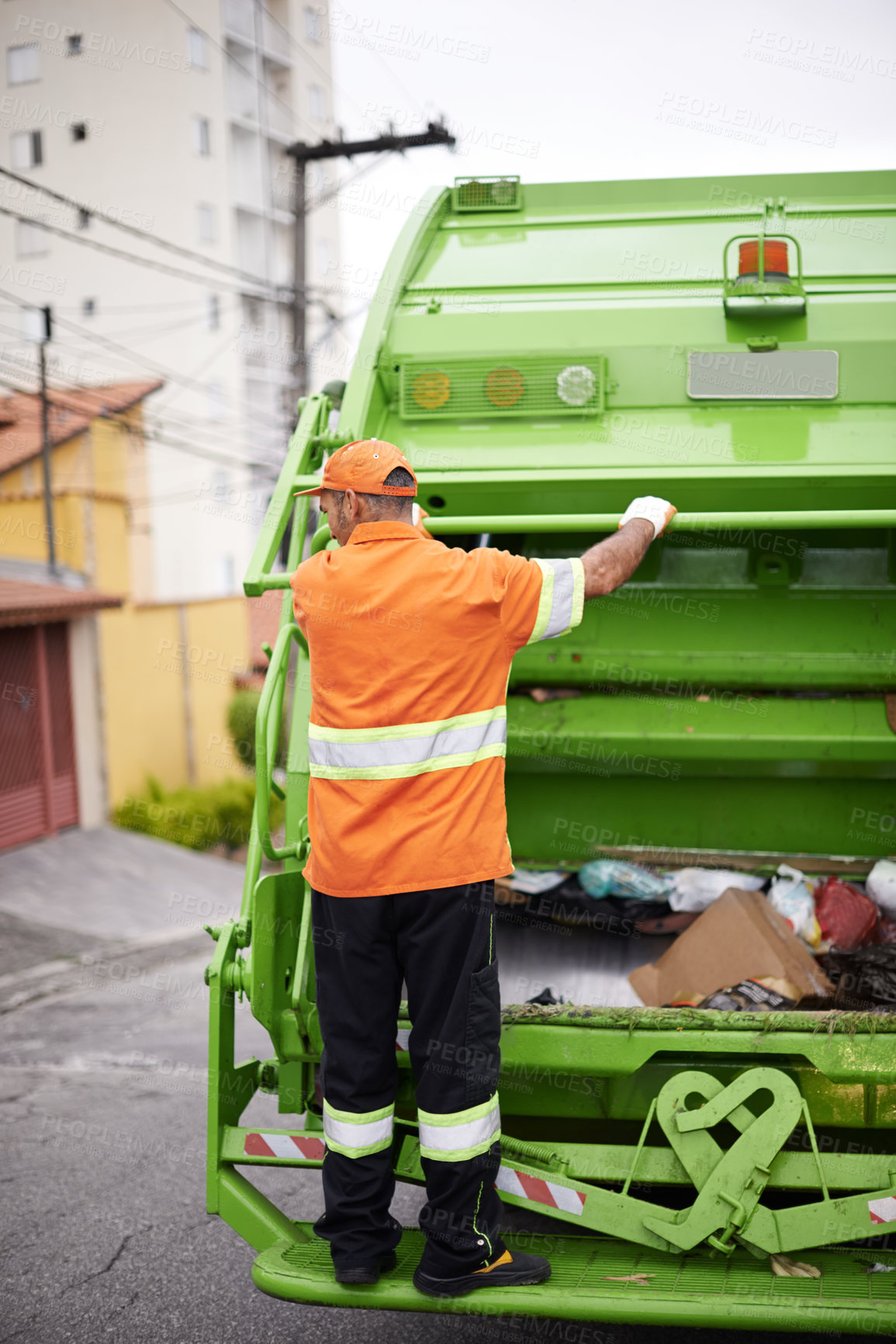 Buy stock photo A garbage collection worker riding on the back of a garbage truck