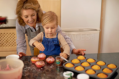 Buy stock photo A little girl decorating cupcakes with the help of her grandmother
