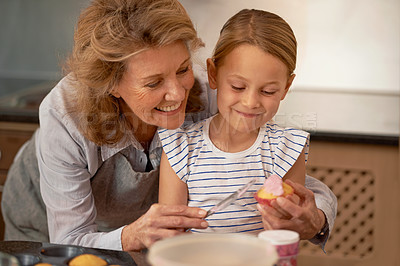 Buy stock photo Shot of a little girl decorating cupcakes with the help of her grandmother