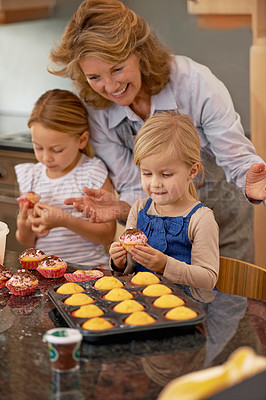 Buy stock photo A grandmother and her two grandchildren decorating cupcakes at home