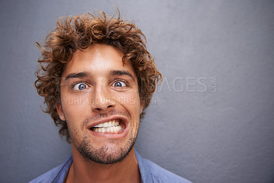 Buy stock photo Young man, portrait and silly face for funny or goofy expression against a gray wall background. Male with crazy humor or impression looking and posing in playful happiness or fun manner and attitude