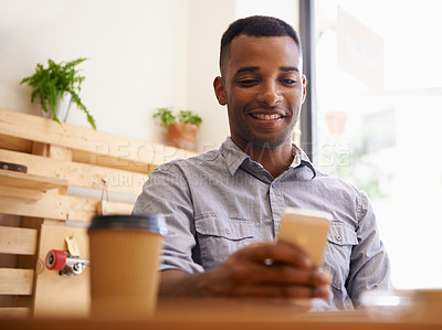 Buy stock photo Cropped shot of a young african man using his smartphone in a coffee shop