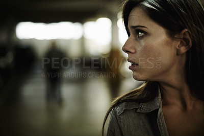 Buy stock photo A young woman in a parking lot looking concerned as someone follows her