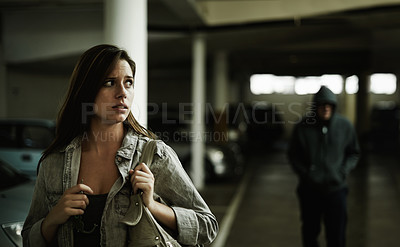 Buy stock photo A young woman in a parking lot looking concerned as someone follows her