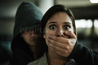 Buy stock photo A terrified young woman held captive by a man with his hand over her mouth