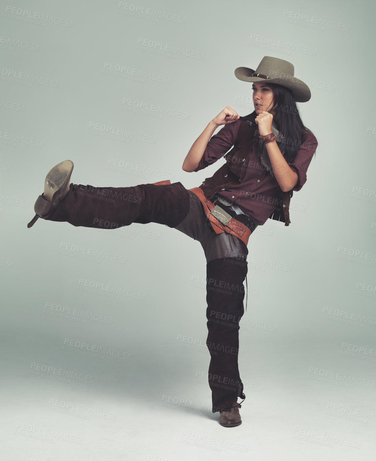 Buy stock photo Cowgirl, kick and fight with fists in studio for western character, wild west outfit and hat for sheriff. Female person, costume and angry with aggression, rage and isolated with grey background