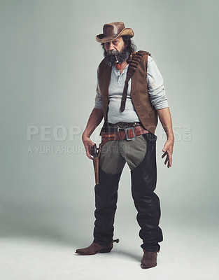 Buy stock photo A grizzled senior cowboy looking confrontational while isolated on gray