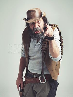 Buy stock photo Senior cowboy, point and angry face at studio, costume and holster for western portrait looking scruffy. Old man, sheriff hat and dirty male for texas, grey background and annoyed gesture for outlaw