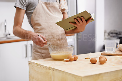 Buy stock photo Cropped shot of a young man cooking in the kitchen with the help of a cookbook