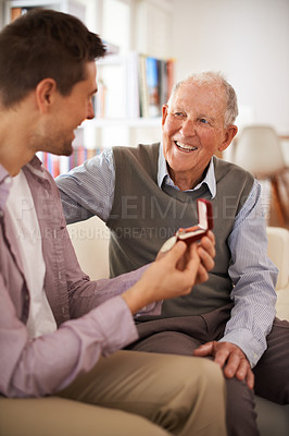 Buy stock photo Dad, adult son and medal for present support and congratulations with celebration and bonding at home. Men in living room, family time with reward or award as gift for happiness and gratitude