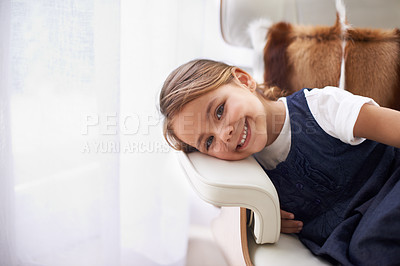 Buy stock photo Happy child, excited and smile for relax, growth and development for childhood in house. Adorable girl, young and healthy kid at home with face expression, comfortable and sitting on armchair at home