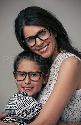 Buy stock photo Happy mother, portrait and hugging daughter with love for care or support in fashion on a gray studio background.  Mom, child or young kid with smile and glasses in happiness for parenting or bonding