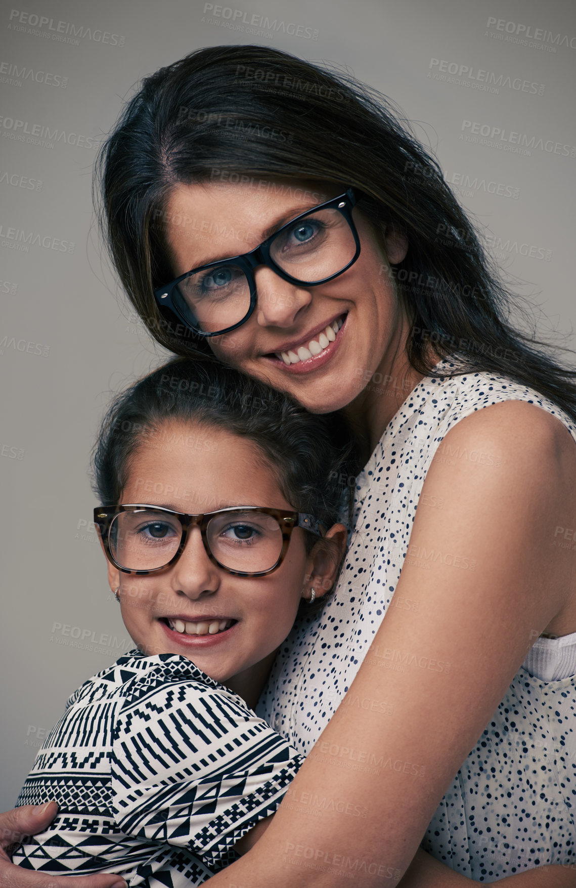 Buy stock photo Happy mother, portrait and hugging daughter with love for care or support in fashion on a gray studio background.  Mom, child or young kid with smile and glasses in happiness for parenting or bonding