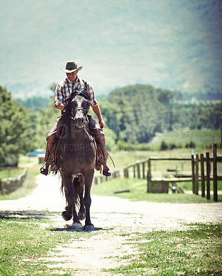 Buy stock photo Shot of a cowboy riding his horse on a country lane