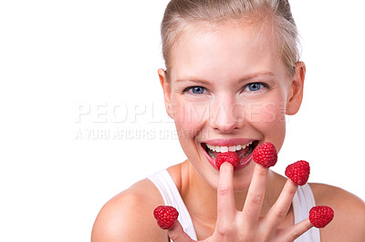 Buy stock photo Shot of a beautiful young woman playfully eating raspberries off her fingertips