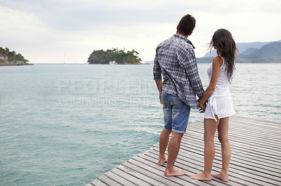 Buy stock photo Couple, jetty and holding hands by ocean on vacation, security and relax by water on holiday. People, travel and bonding for relationship in outdoor, support and back on weekend trip to sea or nature