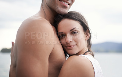 Buy stock photo Portrait of an intimate young couple enjoying a warm embrace by the water's edge
