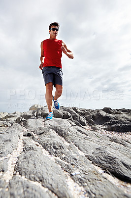 Buy stock photo Male runner, rocky terrain and training, exercising outdoors and seaside for marathon. Fitness, sports and sunglasses for active endurance athlete, health and cardio heart wellness for dedicated man
