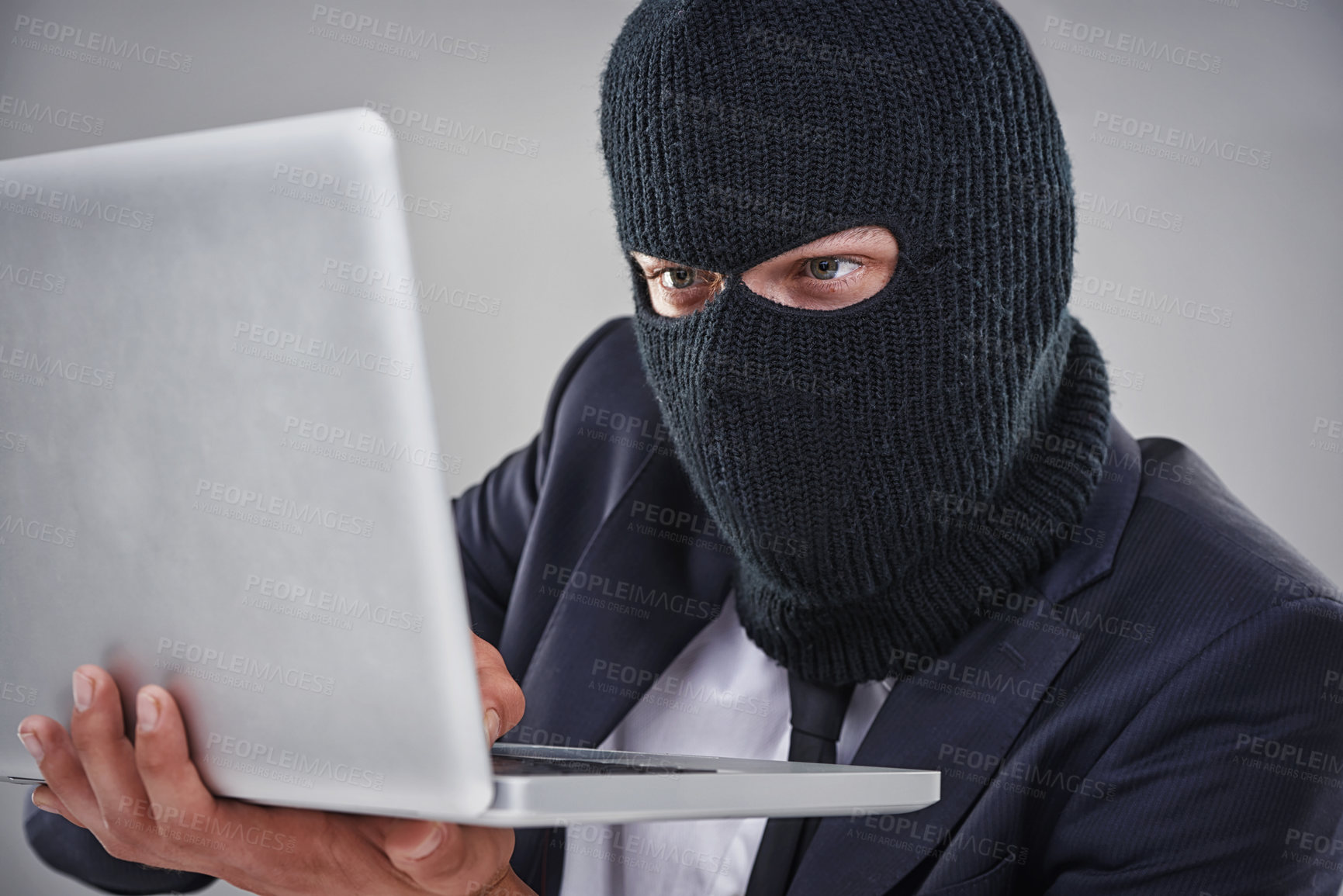 Buy stock photo Conceptual shot of a man with a mask over his head hacking in to a computer