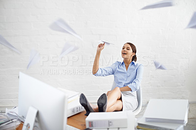 Buy stock photo Shot of a young businesswoman throwing paper planes while sitting at her desk