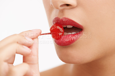 Buy stock photo Cropped studio shot of a beautiful young woman with a cherry between her lips