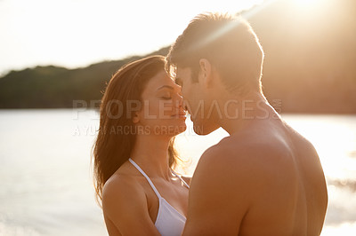 Buy stock photo Love, kiss and couple on island for date on romantic anniversary vacation, adventure or holiday. Smile, bonding and young man and woman embracing with care by ocean at sunset on weekend trip together