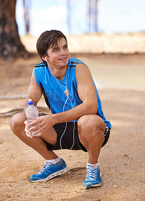 Buy stock photo Shot of a handsome young man taking a break from exercising outdoors