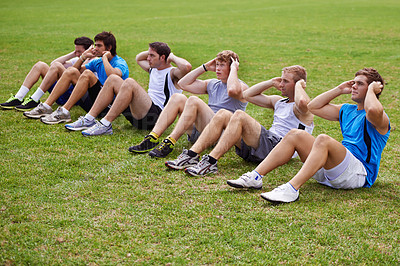 Buy stock photo Shot of a row of young sportsmen doing sit-ups