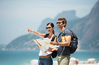Buy stock photo Couple, map and hiking with pointing by mountain, ocean or excited for giving direction on vacation. Woman, man and chart for location, landmark or travel for memory by rocks, sea and nature in Italy