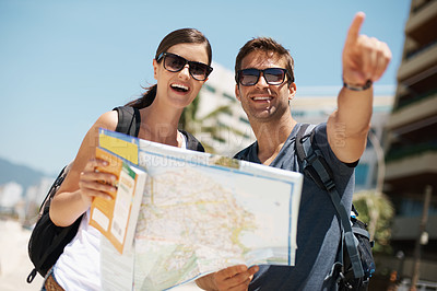 Buy stock photo Couple, map and search with pointing on vacation, street and excited for giving direction. Woman, man and chart for location, landmark and travel for memory with buildings, ocean or nature in Italy