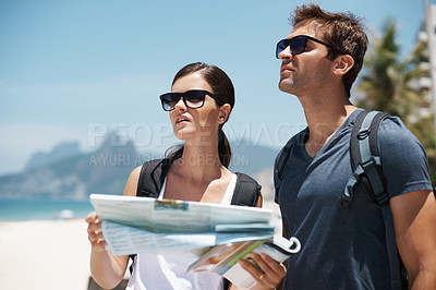 Buy stock photo Shot of a young couple looking at a map while standing on a beach