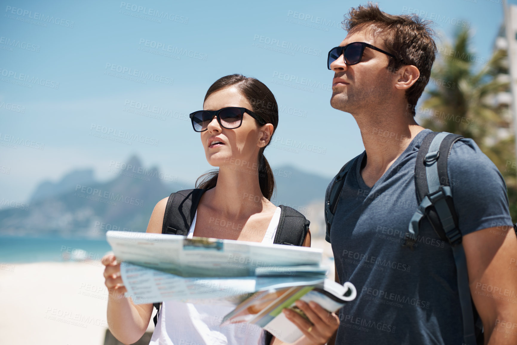 Buy stock photo Shot of a young couple looking at a map while standing on a beach