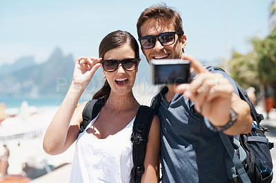 Buy stock photo Couple, beach and camera for selfie on vacation with smile, sunglasses and outdoor for memory in summer. People, man and woman with photography by ocean for journey, vacation and sunshine in Italy