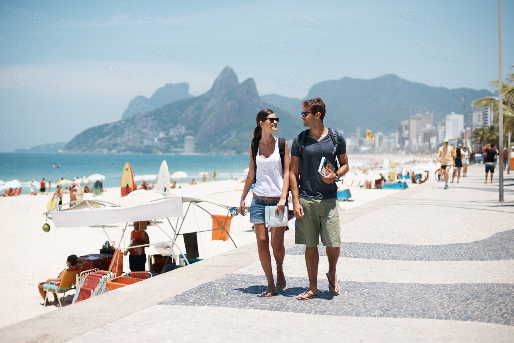 Buy stock photo Cropped shot of a young couple walking along a busy beach