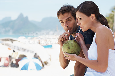 Buy stock photo Young couple enjoying a drink from a coconut while enjoying a day at the beach