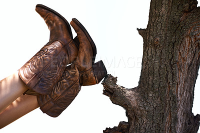 Buy stock photo Cropped shot of a person wearing cowboy boots leaning their feet against a tree