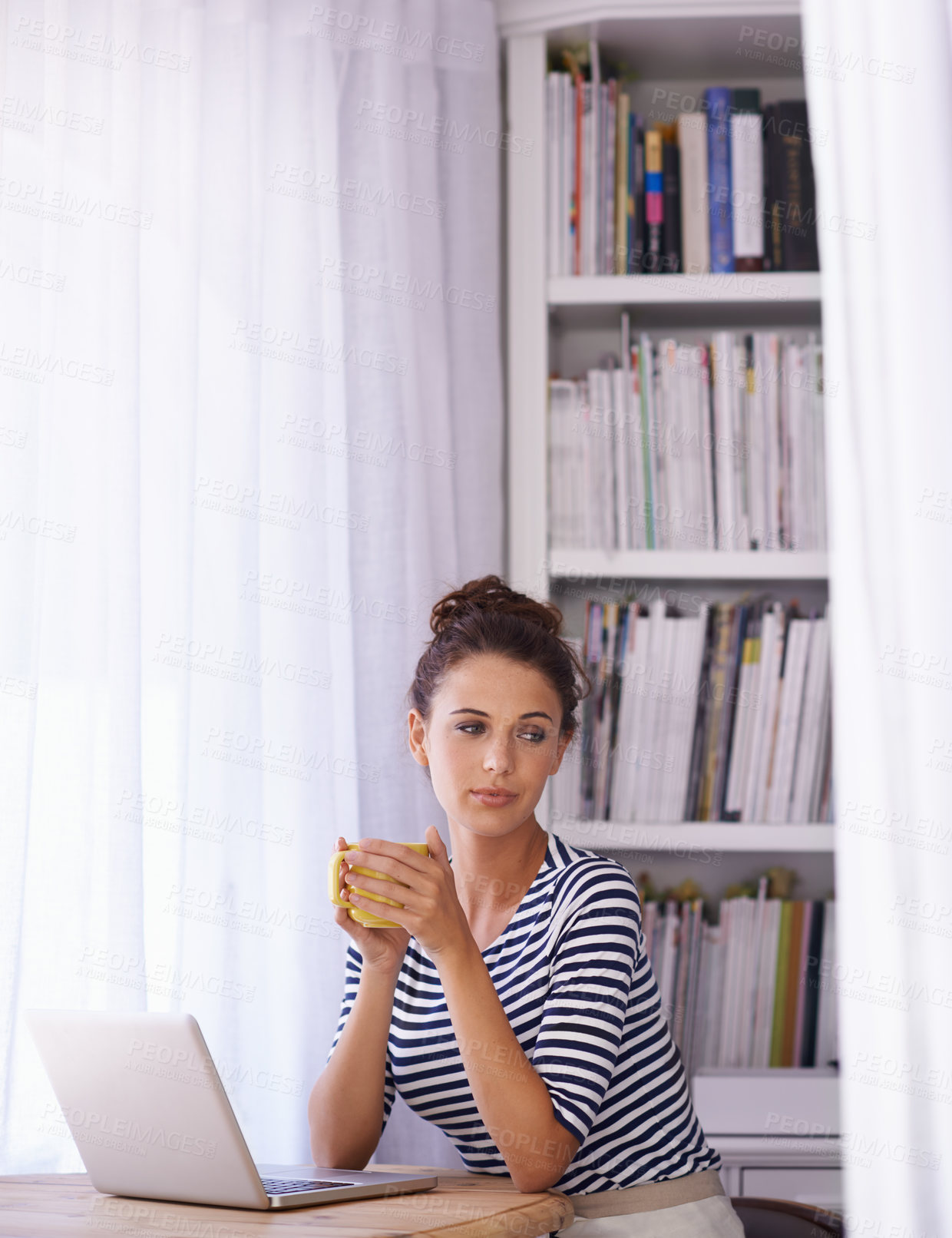 Buy stock photo Shot of a young woman sitting with a laptop and holding a beverage