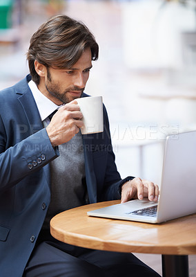 Buy stock photo A handsome businessman working on his laptop and drinking coffee at a coffeeshop