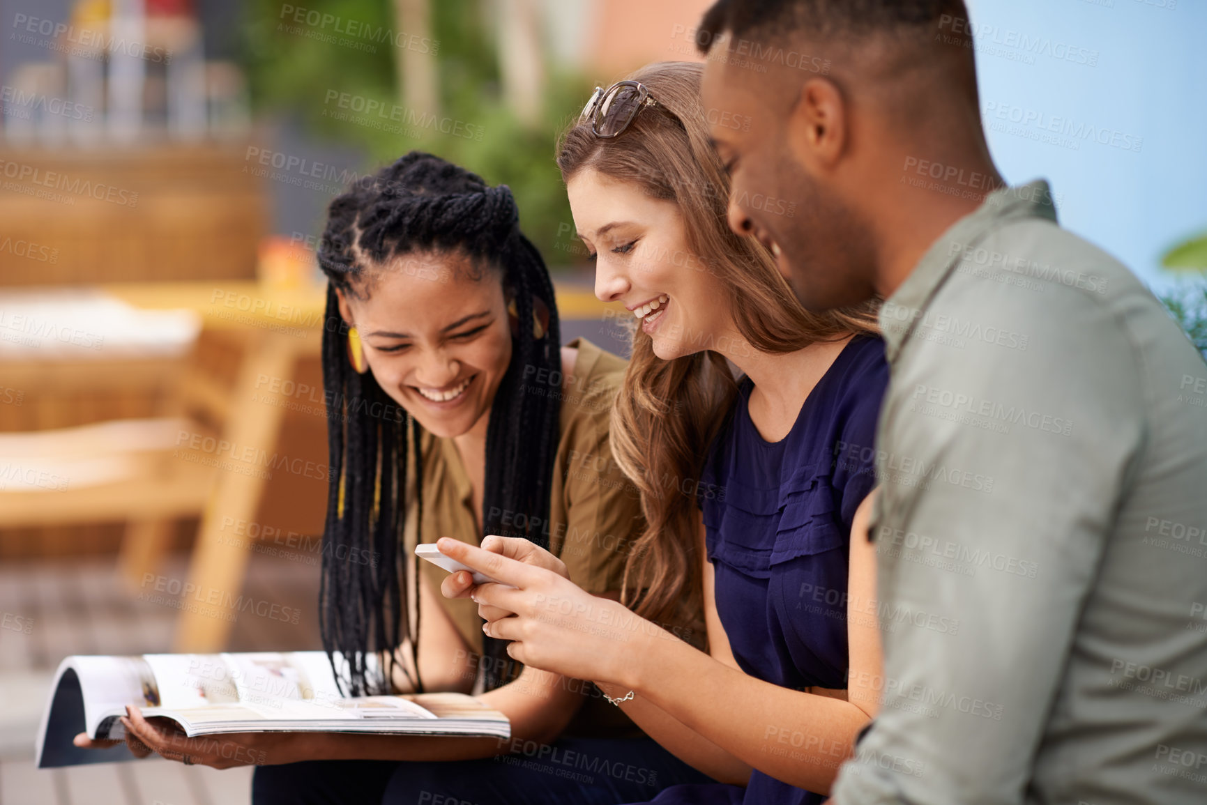 Buy stock photo Three friends reading from a book and a cellphone while sitting outdoors