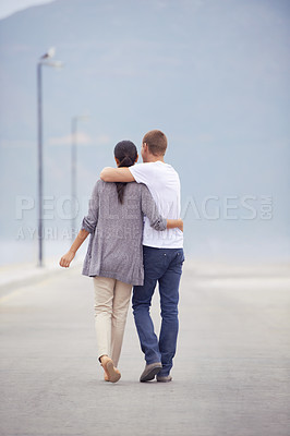 Buy stock photo Full length rearview shot of a young couple walking along a promenade