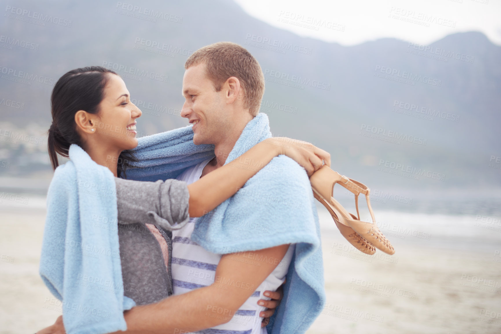 Buy stock photo Happy couple, man and woman on beach with blanket hugging, love and romance in relationship. People, dating and joyful on vacation for holiday, travel and adventure on ocean or sea and mountain view