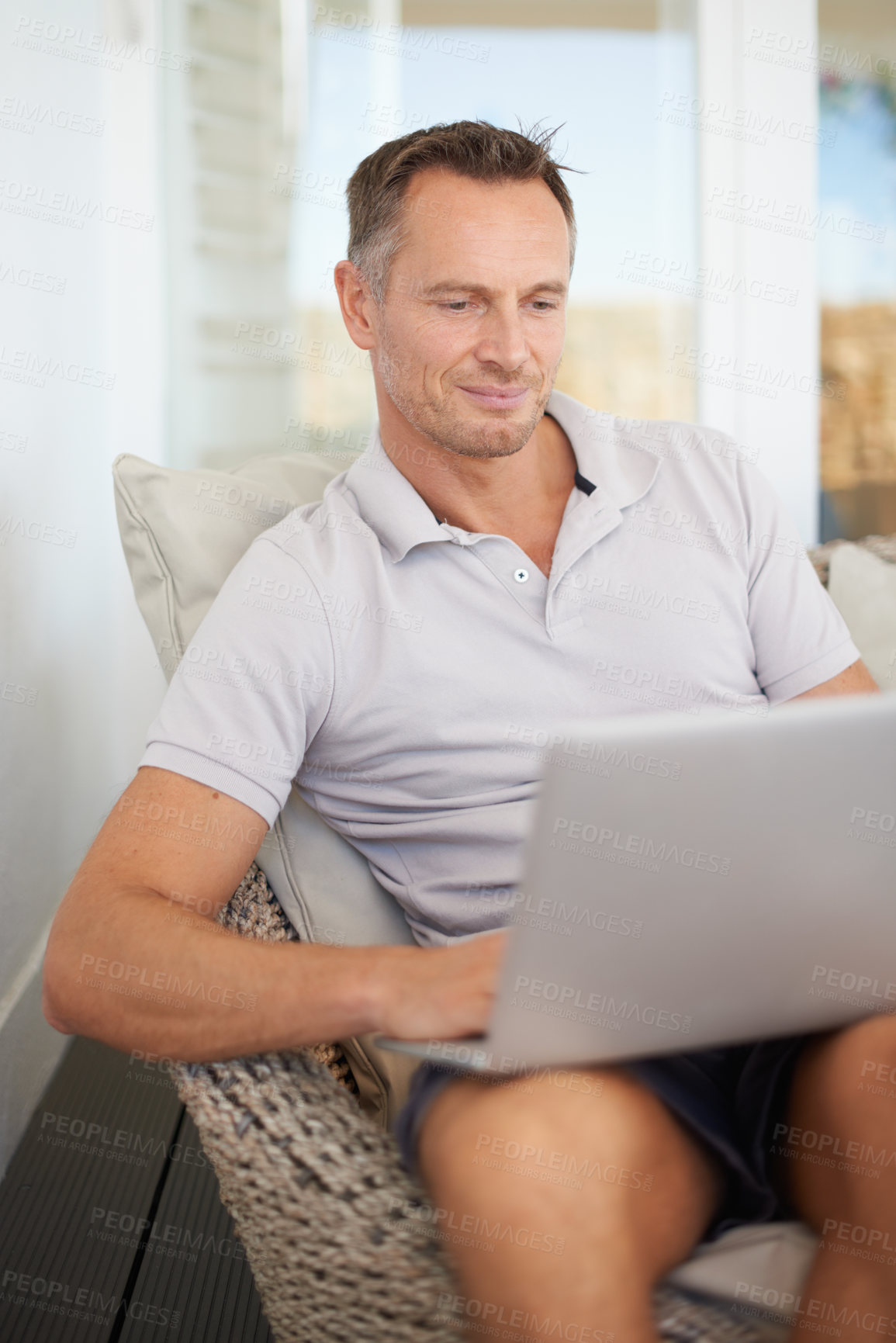 Buy stock photo Man, laptop and relax on patio in home, chair and reading with search for movies on web. Person, computer and happy with thinking, scroll or typing for streaming subscription on holiday at apartment
