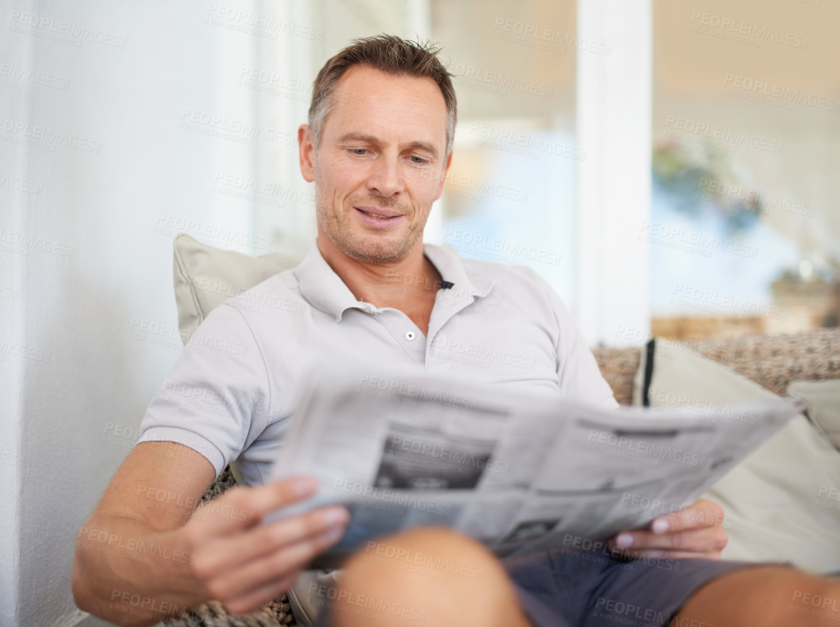 Buy stock photo Man, newspaper and happy for reading on sofa to relax with reading, knowledge and information on patio. Person, newsletter and thinking with update on current affairs, sports and finance at house