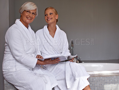Buy stock photo Mother, lady and smile with magazine and robe in bathroom for beauty, skincare and cosmetic treatment. Senior person and daughter on tub in spa with gown and article for wellness, hygiene and care