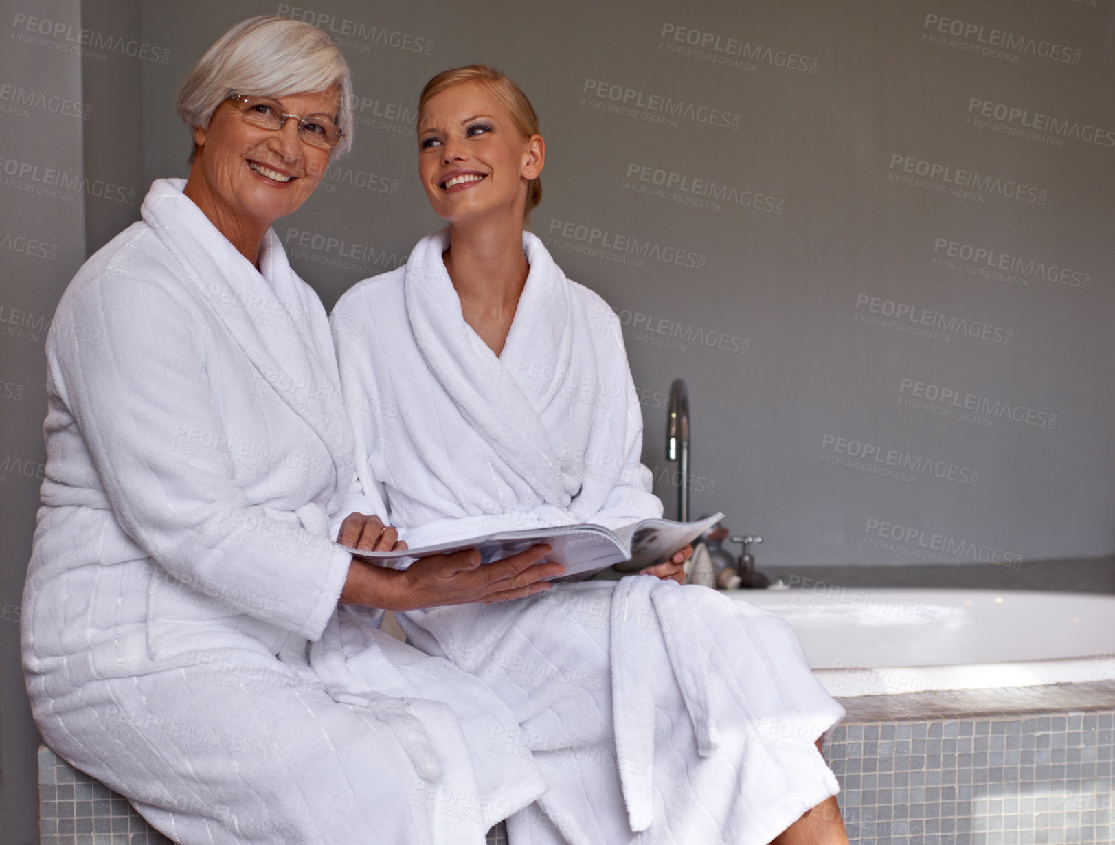 Buy stock photo Mother, lady and smile with magazine and robe in bathroom for beauty, skincare and cosmetic treatment. Senior person and daughter on tub in spa with gown and article for wellness, hygiene and care