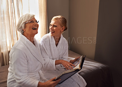 Buy stock photo Grandmother, woman and laughing at photo album, home and happy for bonding and looking at memories. Senior lady, daughter and moment for self care, robe and bedroom for comfort and hospitality 