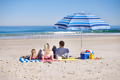 Buy stock photo Family, relax and lying on beach with umbrella for summer holiday, vacation or outdoor weekend together in nature. Rear view of father, mother and daughter chilling on towel or sand by ocean coast