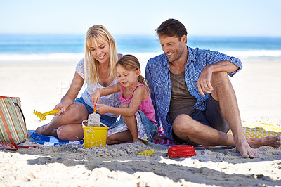 Buy stock photo Mom, dad and girl with sandcastle by sea on vacation with care, learning or building on holiday in summer. Father, mother and daughter with sand in plastic bucket for game, blanket and happy at beach